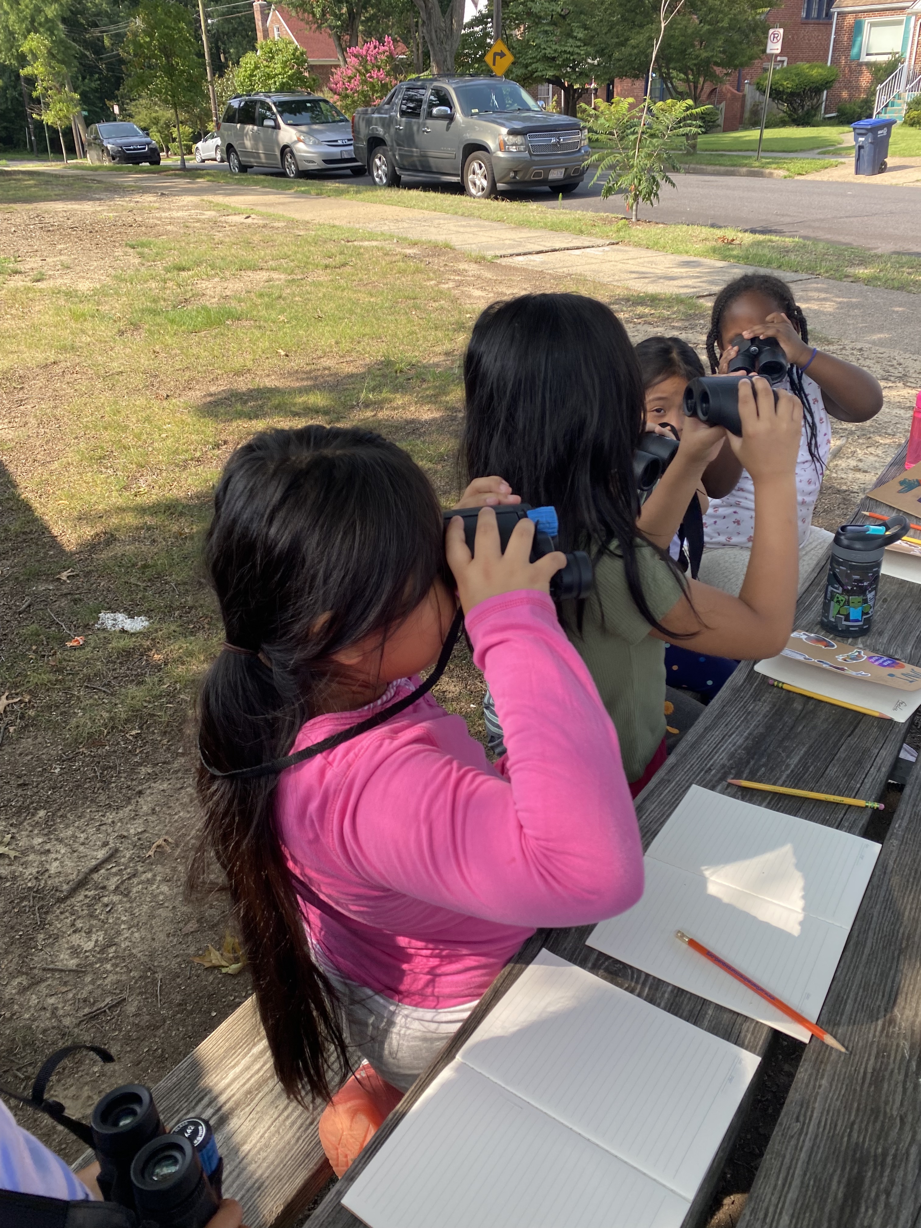 Kids sit at a picnic table and use binoculars to watch birds